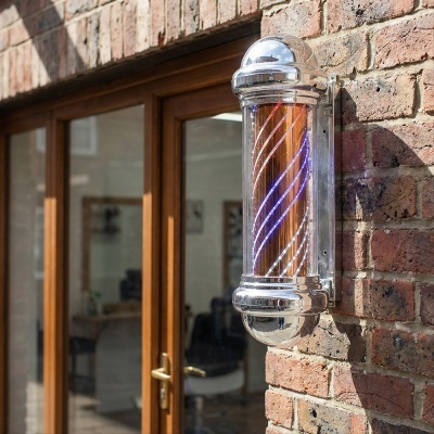 Luminária de parede cromada com LED azul e vermelho em espiral fixa numa parede de tijolos junto a porta de madeira