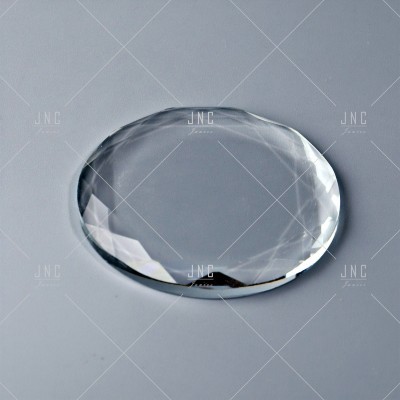 Objeto oval transparente com bordas facetadas sobre superfície cinza
