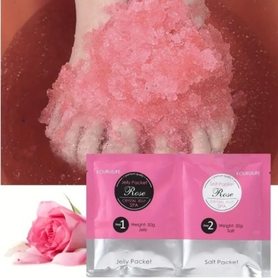 Pé com cristais de sal rosa em água cor-de-rosa e pacotes de spa Rose Jelly e Salt