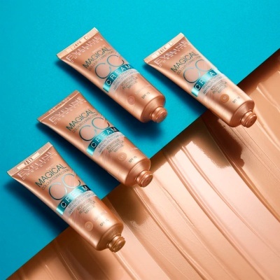 Quatro tubos de creme facial Maybelline Magica CC Cream sobre fundo azul com creme espalhado