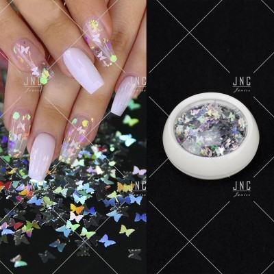 Unhas decoradas com adesivos holográficos de borboleta e recipiente com adesivos similares