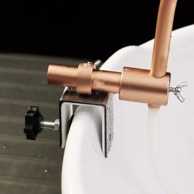 Suporte metálico com parafuso preto e acessório de cobre fixado a borda curva branca com mangueira translúcida