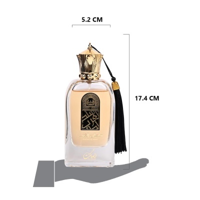 Frasco de perfume ouro e vidro com tassel preto sobre mão cinza