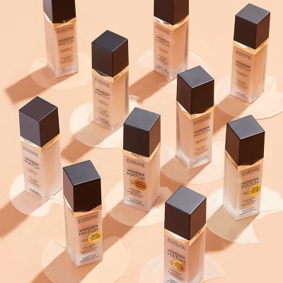 Frascos de base de maquilhagem líquida Revolution com tampa preta dispostos em padrão sobre fundo bege.