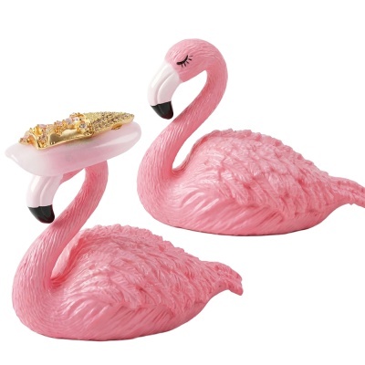 Suportes decorativos rosas em forma de flamingo com um deles segurando anel dourado com pedras