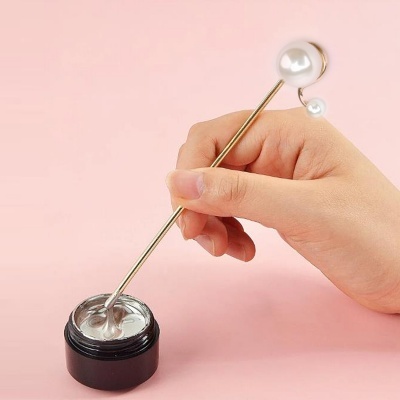 vareta dourada com pérolas a ser mergulhada num pote de creme branco