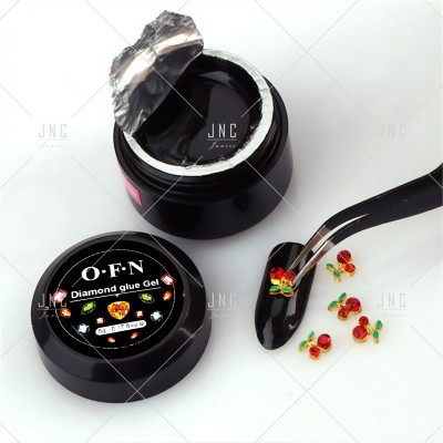 Frasco de gel preto para unhas com decorações coloridas ao lado e pinça