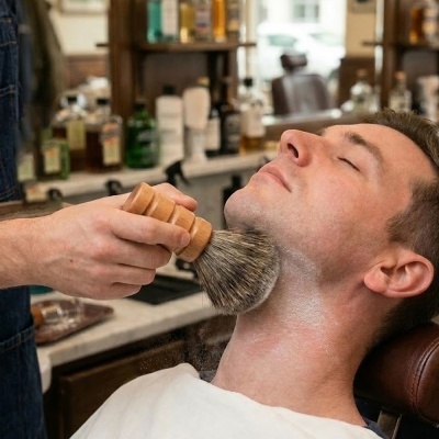 Escova de barbear com cabo de madeira a ser utilizada no pescoço de um homem numa barbearia