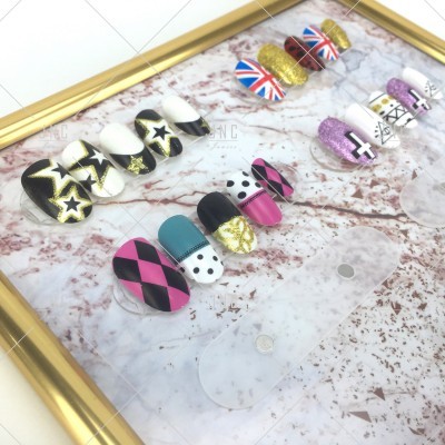 Unhas postiças decoradas com vários padrões coloridos colocadas sobre uma superfície marmoreada dentro de uma moldura dourada.