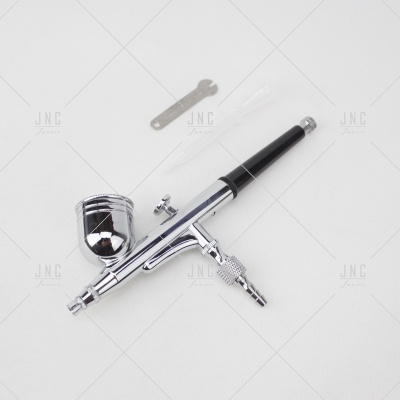 Aerógrafo prateado com detalhes pretos e ferramentas auxiliares sobre fundo branco