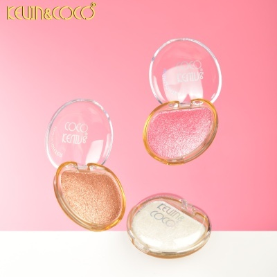 Maquilhagens iluminadoras KEVIN&COCO dourado, rosa e branco em embalagens redondas transparentes em fundo rosa.