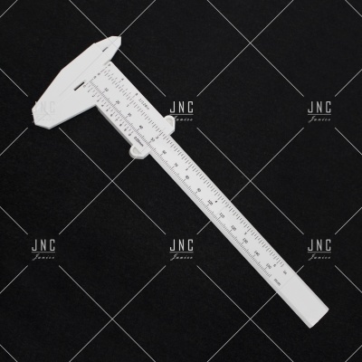 Paquímetro branco de plástico com escala em milímetros sobre fundo preto