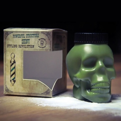 Frasco verde em forma de caveira ao lado de caixa de papelão com texto e gráfico vintage