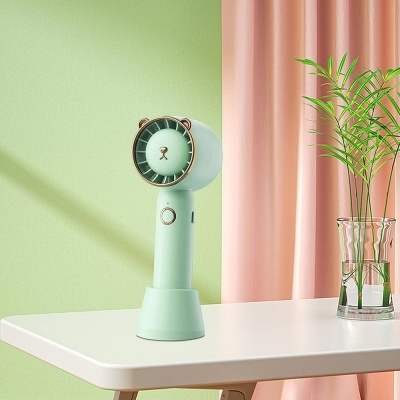 Ventoinha portátil verde claro em mesa branca com planta e cortinas cor-de-rosa