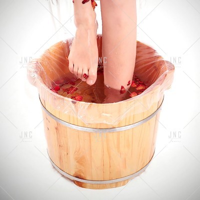 Pés femininos dentro de balde de madeira com água e pétalas vermelhas