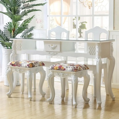 Mesa branca clássica com tampo de vidro e bancos com estofos florais num ambiente interior claro