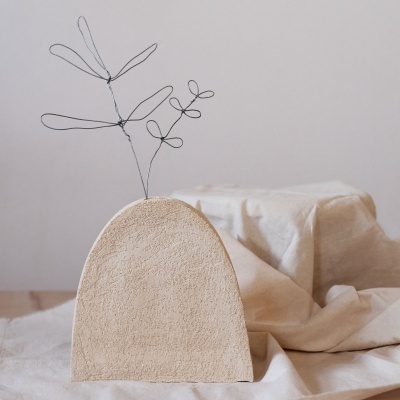 Vaso semicircular bege com decoração de arame em forma de folhas sobre tecido bege