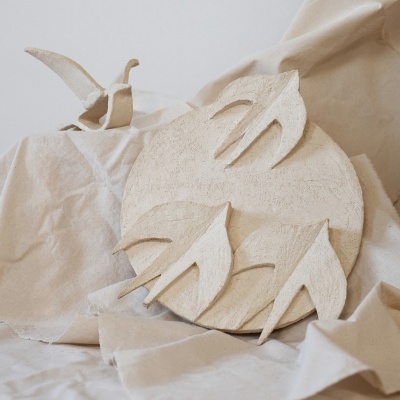 Escultura decorativa de cerâmica com andorinhas em relevo e base circular sobre tecido bege