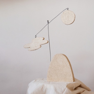 Escultura decorativa com móbil de nuvem e círculo suspensos em fios pretos sobre base bege texturizada