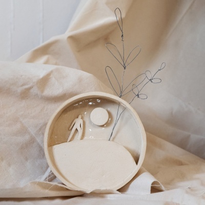 Escultura decorativa redonda com figura humana e arame em forma de folhas sobre tecido bege