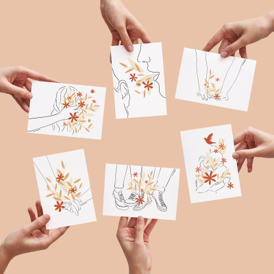 Cartões com ilustrações de corpos e flores segurados por mãos sobre fundo rosa