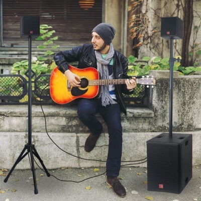 Homem sentado a tocar guitarra acústica laranja e preto ao ar livre com altifalantes e subwoofer negros