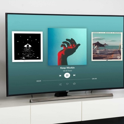 Televisão plana com música e duas colunas pretas sobre móvel branco