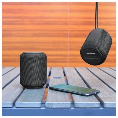 Colunas portáteis pretas Tronsmart e smartphone numa mesa de madeira