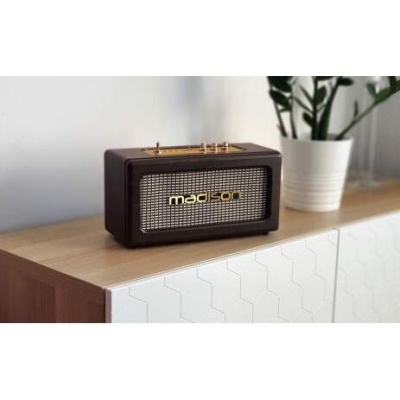 Aparelho de rádio retro preto com grelha metálica e texto 'madison' sobre móvel de madeira junto a um vaso branco com planta.