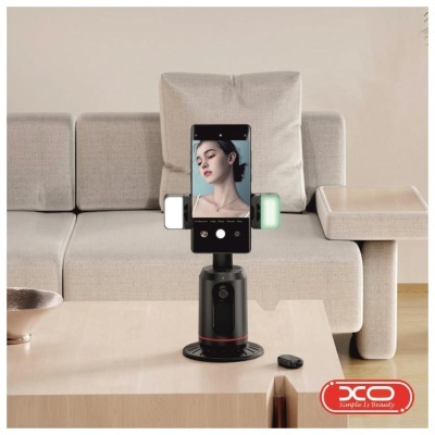 Suporte telefónico automático preto com telemóvel em mesa de madeira e sofá cinzento ao fundo