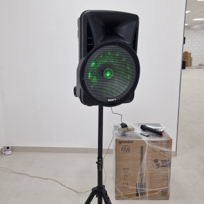 Coluna de som preta num tripé com luz verde, caixa Gemini WPX-3000 e microfone neste espaço interior.