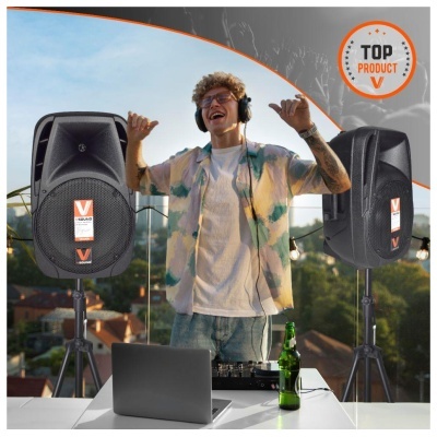 DJ entre colunas de som pretas ao ar livre com mesa, garrafa verde e laptop cinzento