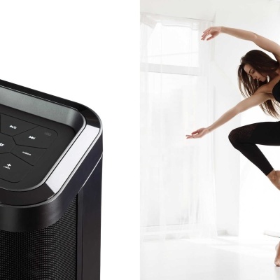 Coluna de som preta com painel tátil e mulher a dançar em roupa desportiva preta numa sala iluminada.