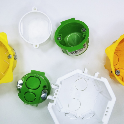 Caixas de derivação elétricas amarelas, verdes e brancas com tampas e parafusos sobre fundo branco