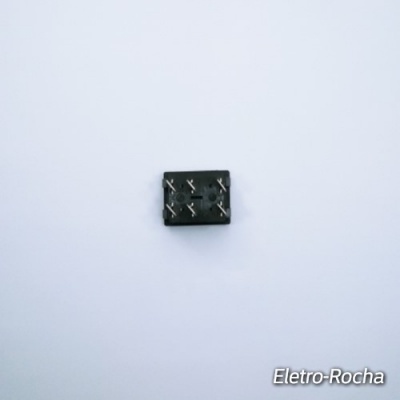 Conector elétrico preto com seis pinos metálicos numa superfície branca