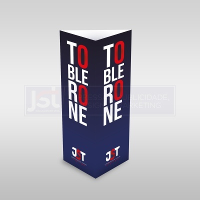 Display publicitário tríptico azul escuro com texto 'TOBLERONE' em branco e vermelho e logótipo JST