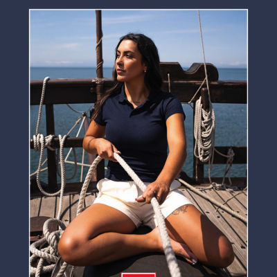 Mulher sentada num convés de barco com roupa casual, capa de catálogo CATÁLOGO 2025