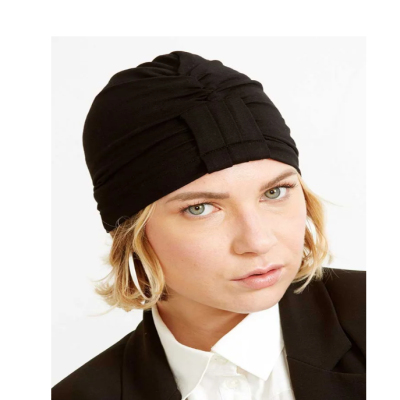 Mulher com turbante preto, brincos largos, blazer e camisa branca.