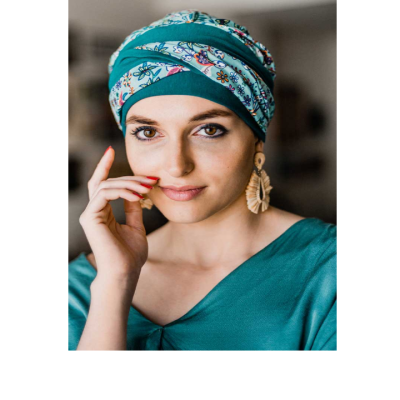 Mulher com turbante azul e branco floral, blusa azul turquesa e brincos de tecido grandes