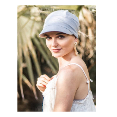 Mulher com chapéu cinza claro e blusa branca em ambiente exterior com plantas