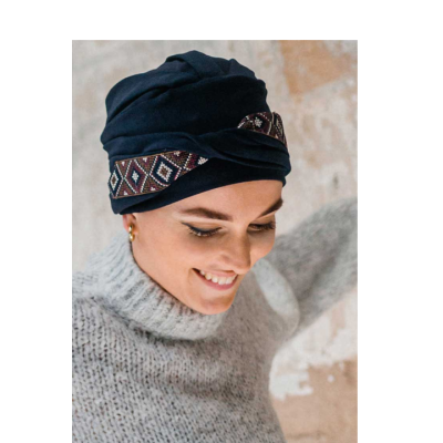 Mulher a usar turbante preto com padrão geométrico e casaco cinzento de malha