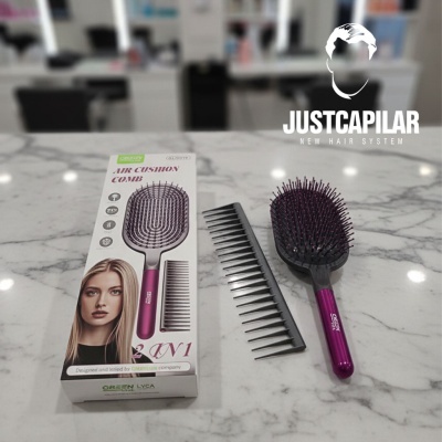 Escova de cabelo air cushion rosa com pente preto e embalagem sobre mármore cinza claro.
