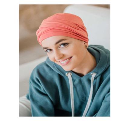 Mulher com lenço cor-de-rosa claro e sweat azul esverdeado sentada num sofá