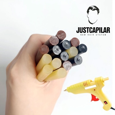 Mão segurando bastões de parafina coloridos e pistola de cola quente amarela junto a logótipo