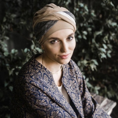 Mulher com turbante bege e casaco com padrão floral azul e dourado