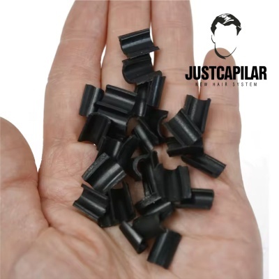 Mão com pequenas peças pretas de plástico curvado e logo JUSTCAPILAR