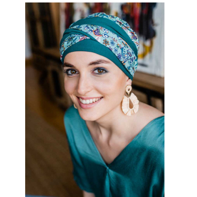 Mulher com lenço turquesa com padrão floral colorido na cabeça e brincos grandes.