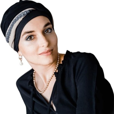 Mulher com lenço preto e bege, colar e brinco de pérolas, e blusa preta