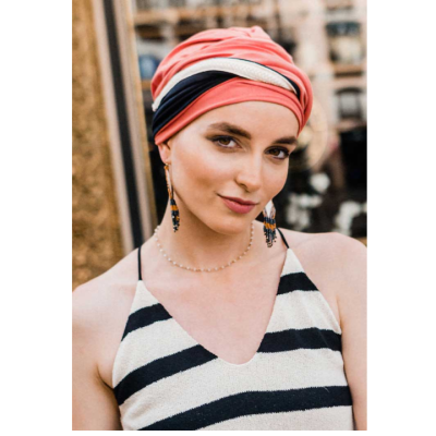 Pessoa jovem com turbante laranja, rosa e preto, vestido às riscas e acessórios coloridos.