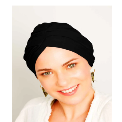 Mulher com turbante preto, brincos dourados e blusa branca em fundo claro